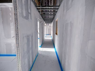 Langer Rohbauflur mit unverputzten W&auml;nden und freiliegenden Kabeln an der Decke, zeigt Innenausbauphase.