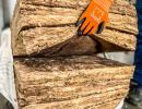 Hand mit orange Handschuh h&auml;lt Glaswolle-Isolierung, zeigt Material zur W&auml;rmed&auml;mmung von Geb&auml;uden