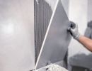 Person setzt gro&szlig;e graue Wandfliese mit Kleber ein, tr&auml;gt Handschuhe, pr&auml;zise Arbeit bei Fliesenverlegung sichtbar