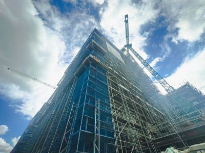 Hohes Geb&auml;ude einger&uuml;stet, Kr&auml;ne arbeiten daran, zeigt Fortschritt im Hochbau unter blauem Himmel mit Wolken